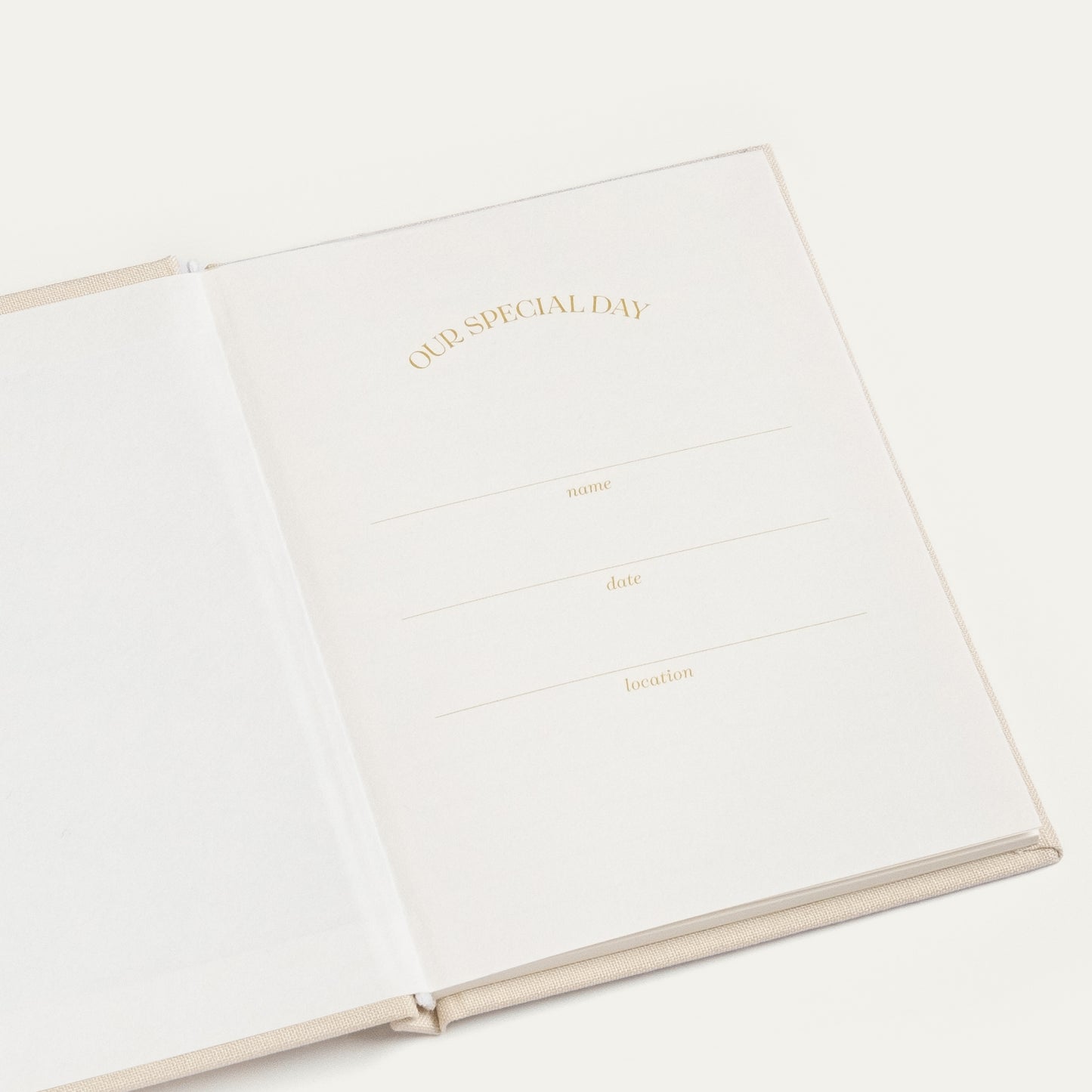 An open cream-colored hardcover journal or notebook with elegant gold foil text reading 'OUR SPECIAL DAY' and lines for writing date, name, and location, set against a clean off-white background.