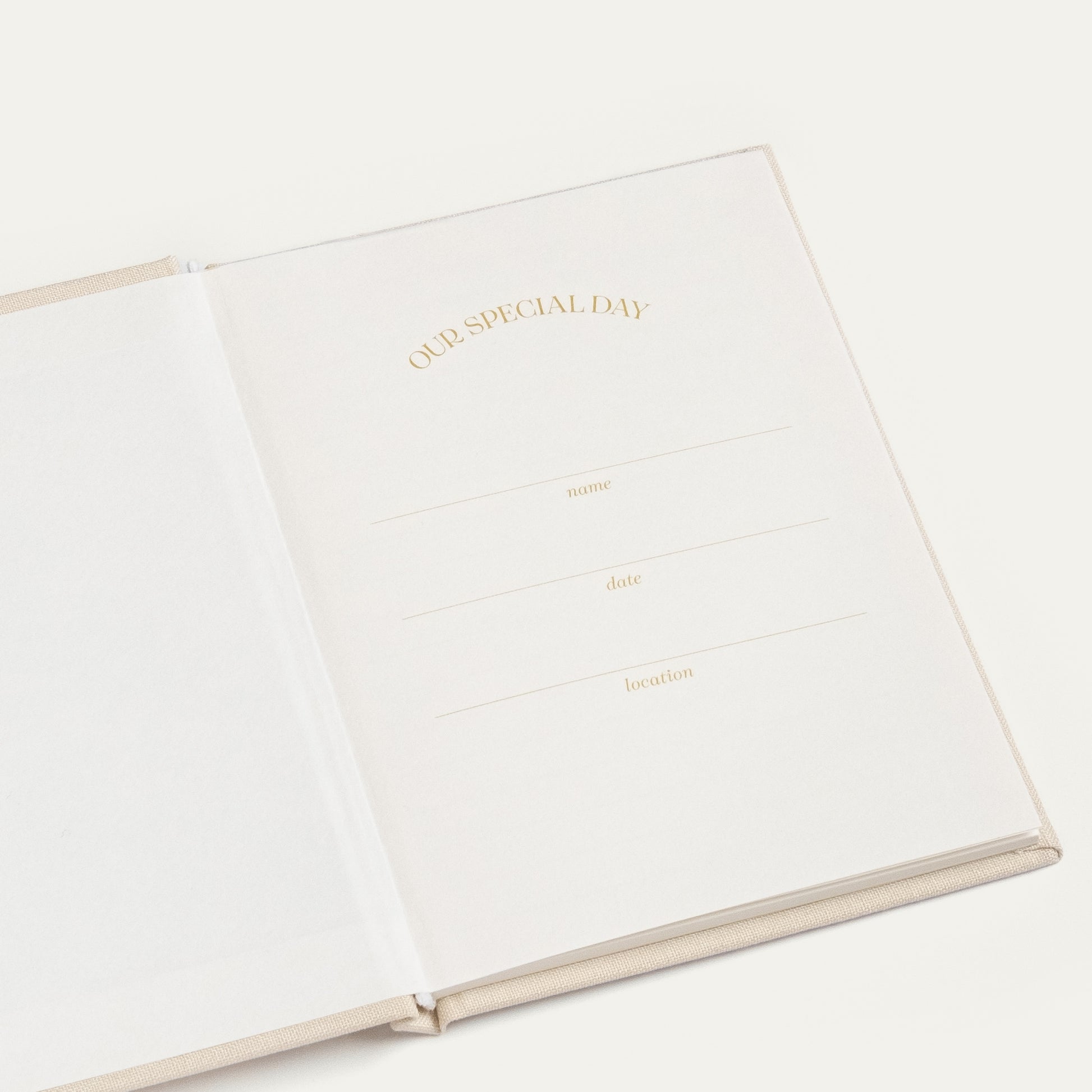 An open cream-colored hardcover journal or notebook with elegant gold foil text reading 'OUR SPECIAL DAY' and lines for writing date, name, and location, set against a clean off-white background.