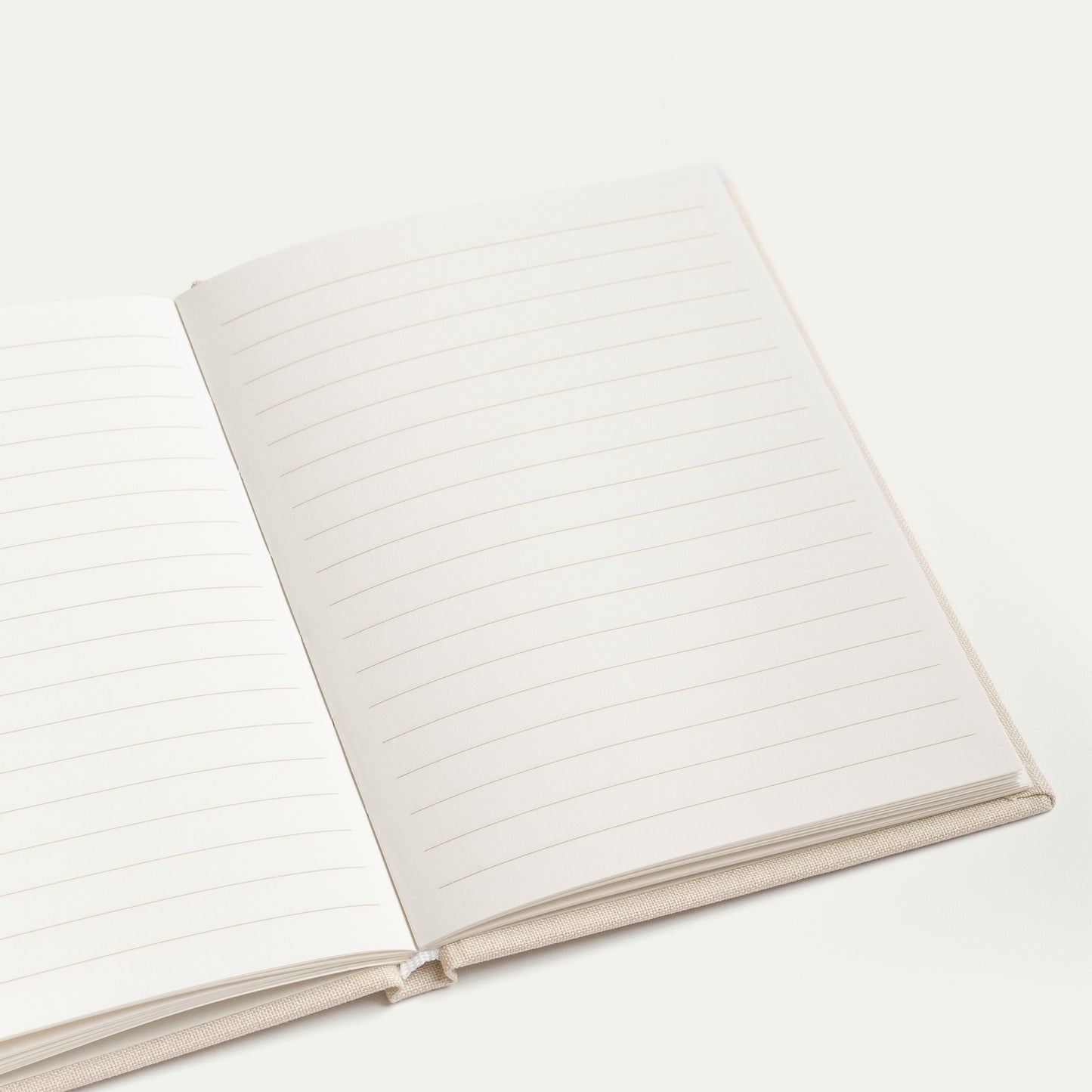 An open lined vow book with blank white pages and a light beige fabric cover, photographed on a clean off-white background.