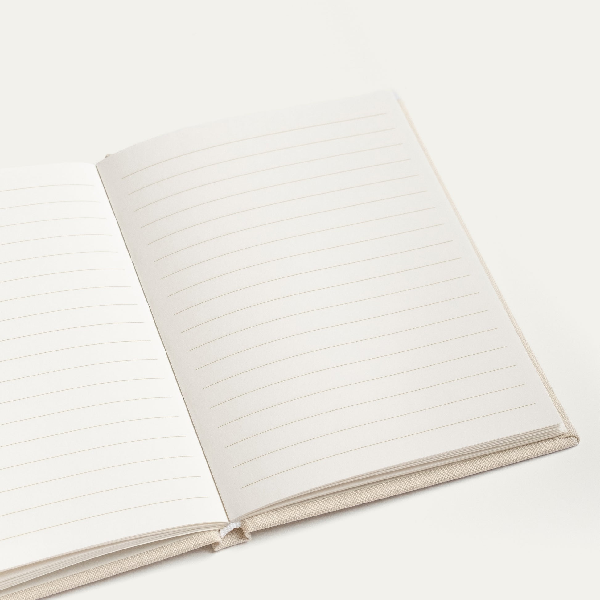 An open lined vow book with blank white pages and a light beige fabric cover, photographed on a clean off-white background.