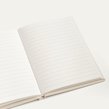 An open lined vow book with blank white pages and a light beige fabric cover, photographed on a clean off-white background.