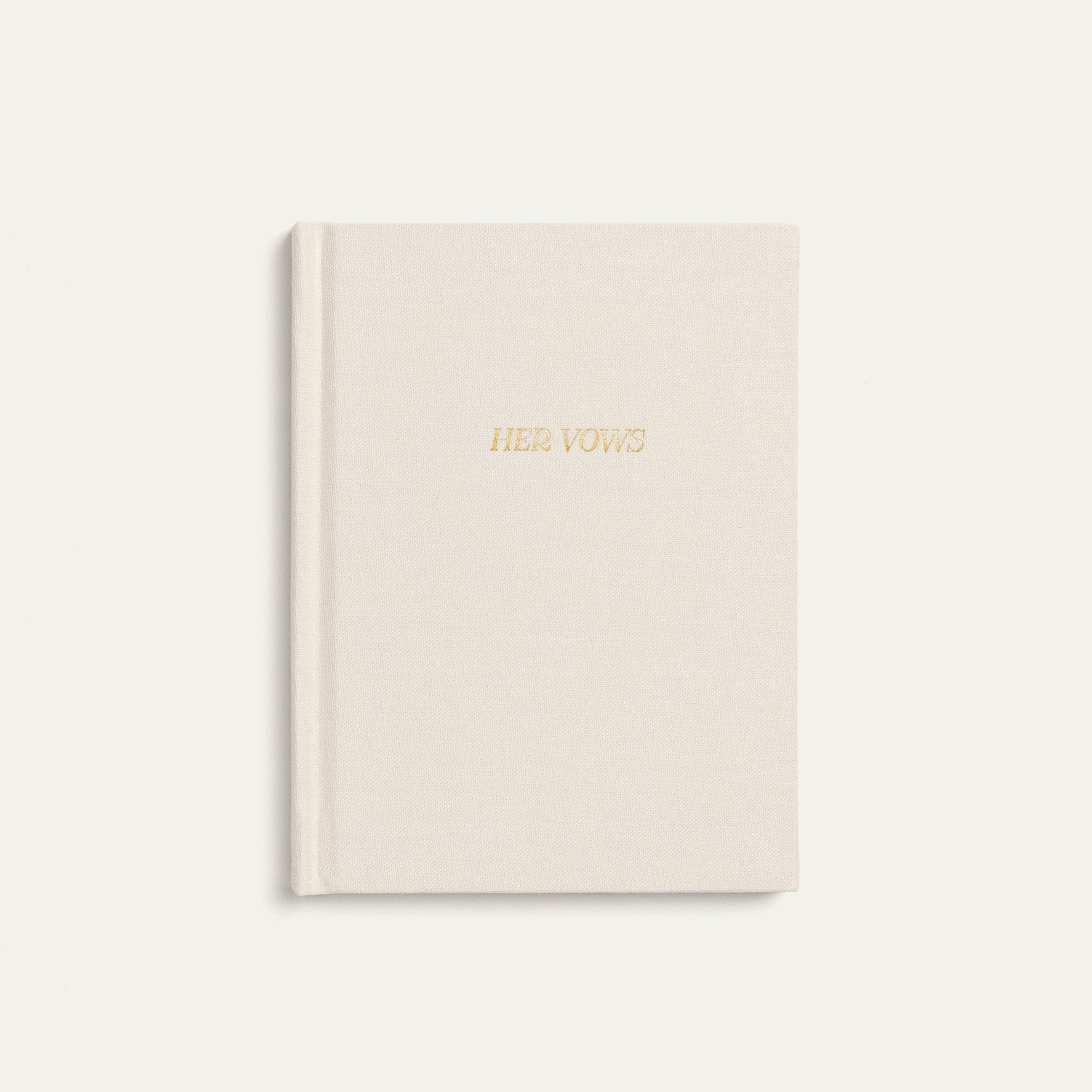 A cream-colored hardcover vow book with 'HER VOWS' embossed in gold foil on the front cover, set against a matching cream background.