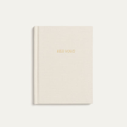 A cream-colored hardcover vow book with 'HER VOWS' embossed in gold foil on the front cover, set against a matching cream background.